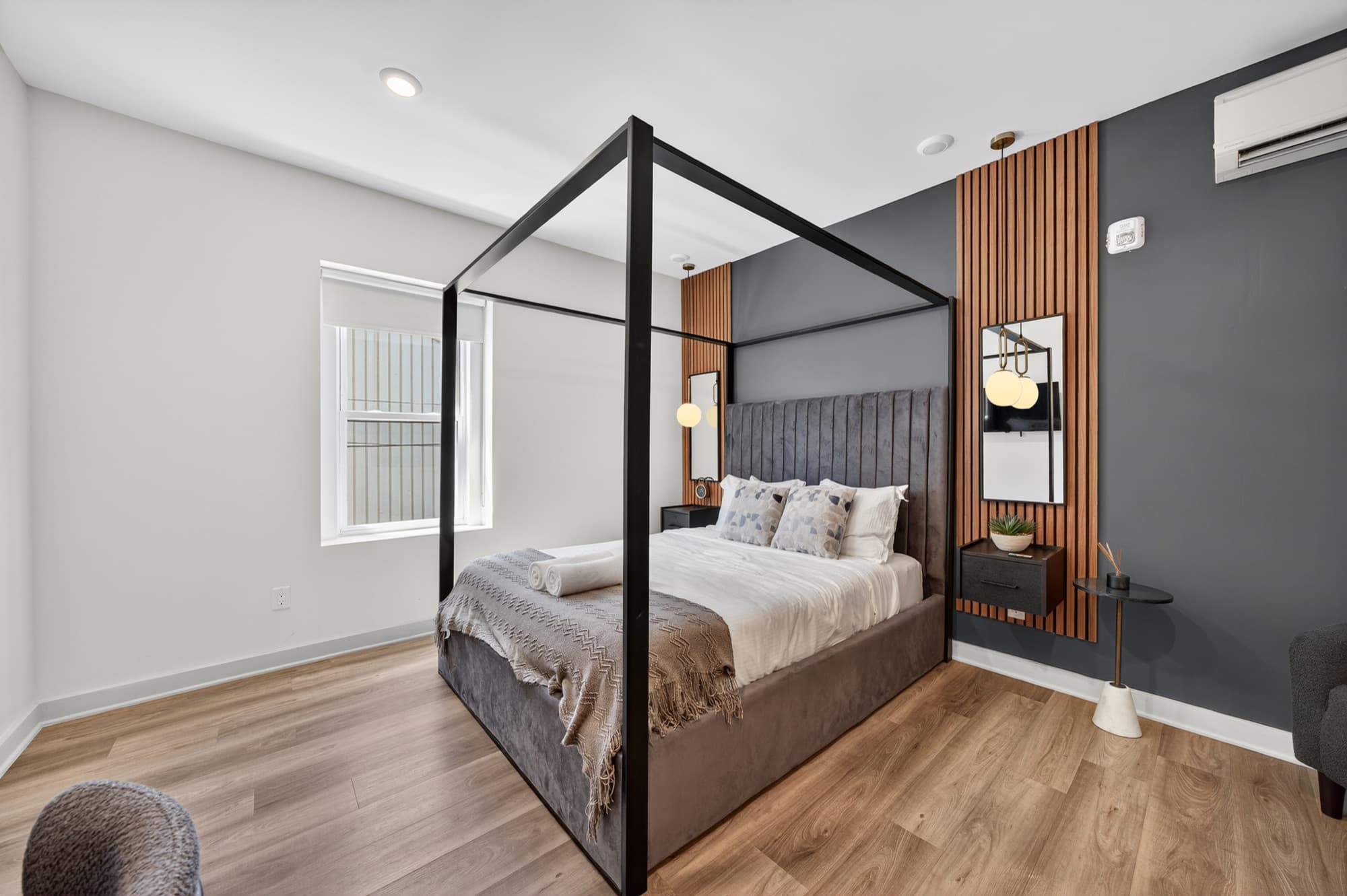 The Balcony Suite at 52 Cottage Street: a black four-poster bed in white linen against a dark wall with a wood-slat panel, a window on the left.